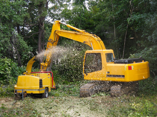 tree lopping mandurah's digger in a clearing of trees with a wood chipper spitting out wood chippings